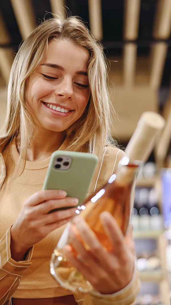 A joyful woman engaging with her smartphone, her smile showing healthy teeth, set against a contemporary backdrop with wooden beams overhead.