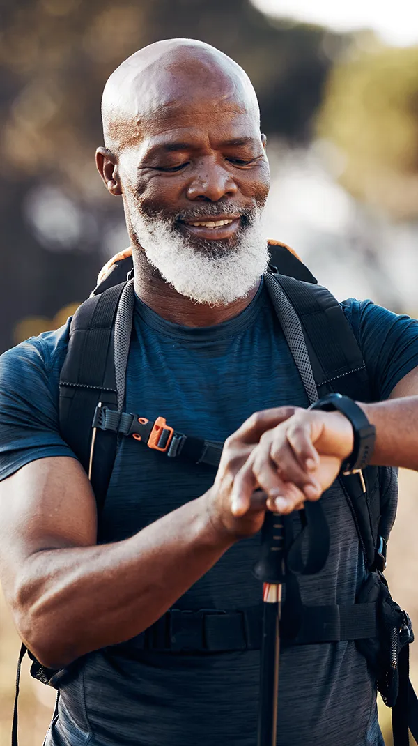 Smiling elderly man with a beard adjusting his watch while hiking, showcasing his vibrant and healthy smile in an outdoor setting, symbolizing an active lifestyle post full mouth reconstruction.